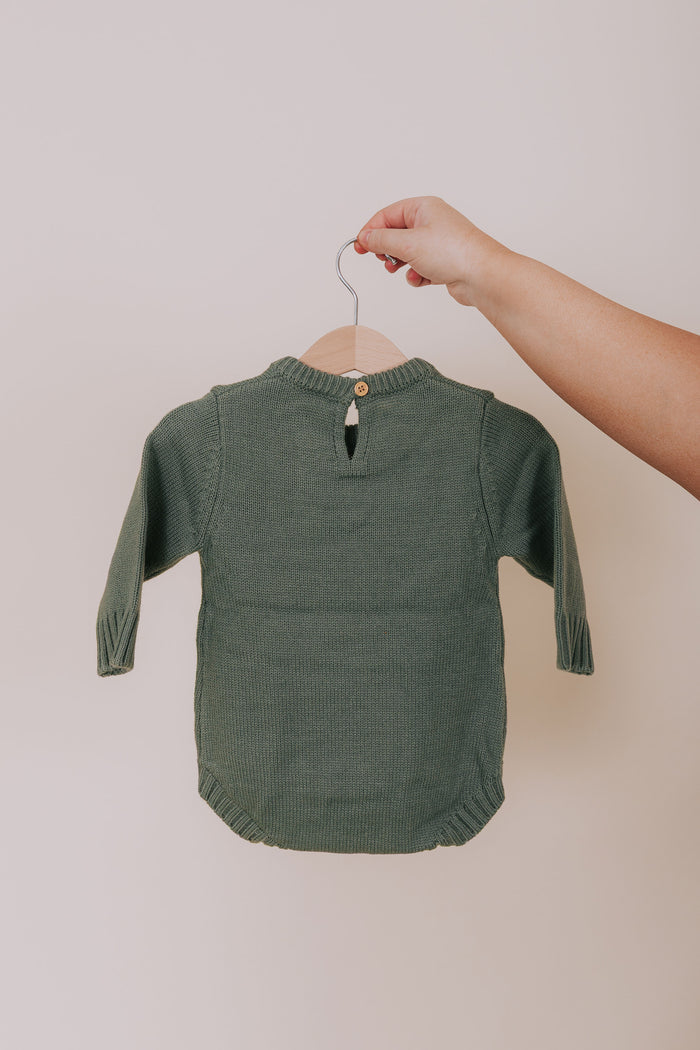 Green baby romper on a hanger against a plain background
