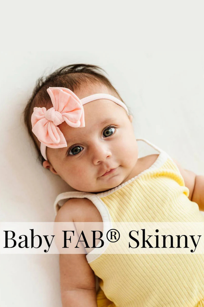 Baby wearing a yellow outfit and pink headband with 'Baby FAB® Skinny' text.