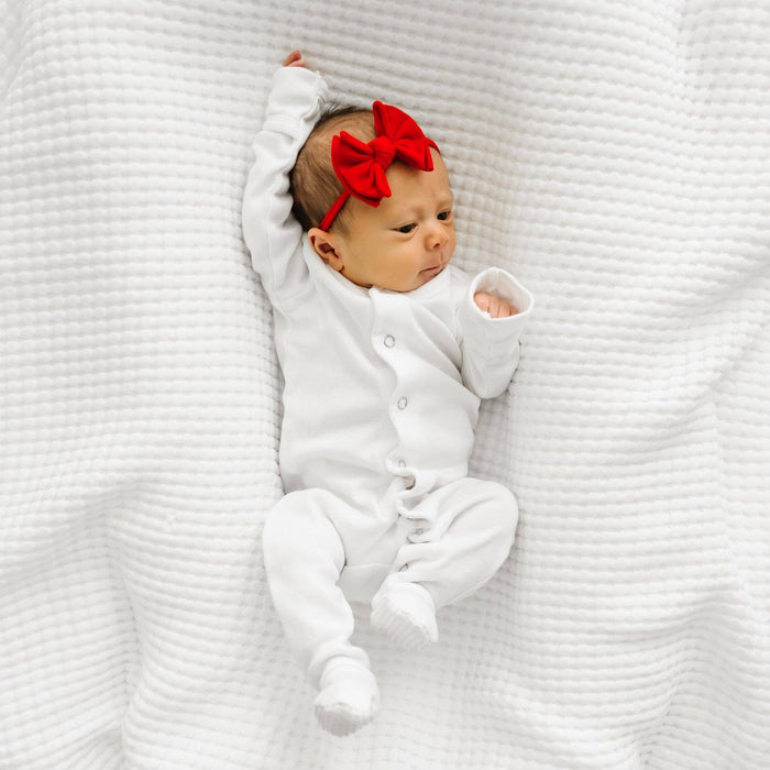 Newborn baby in a white outfit with a red bow on a white textured blanket