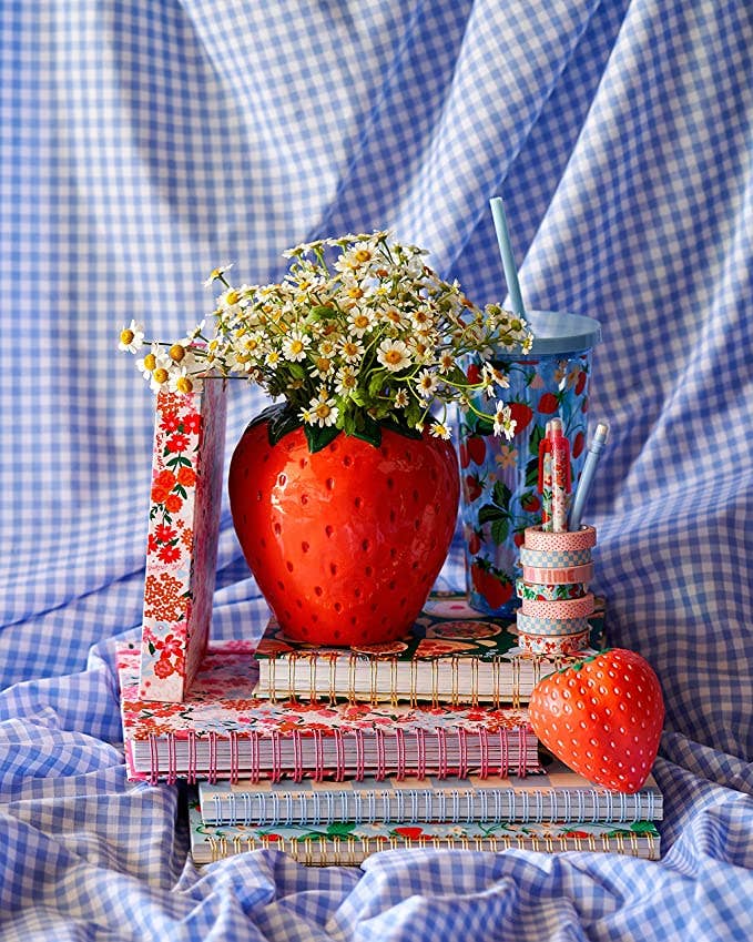 Decorative setup with strawberry-themed items on a blue checkered fabric background strawberry shaped vase holding flowers red