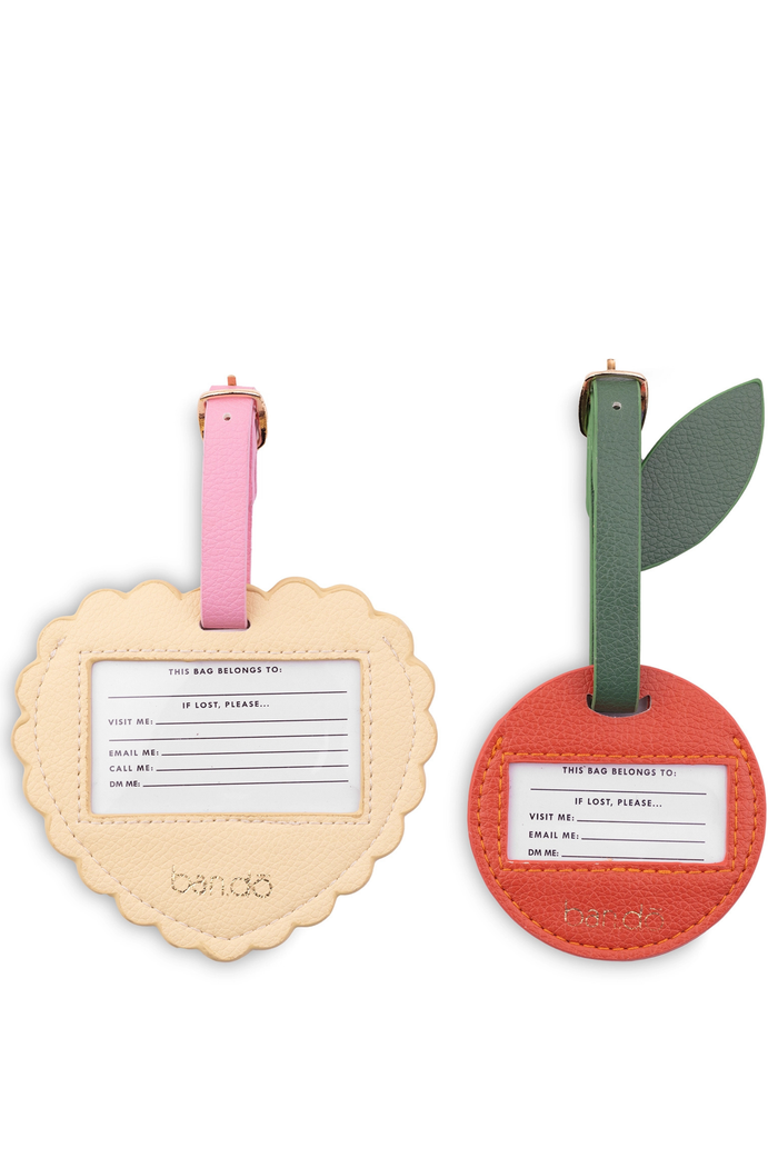Two luggage tags, one beige with a pink strap and one red with a green strap, on a white background. heart and cherry