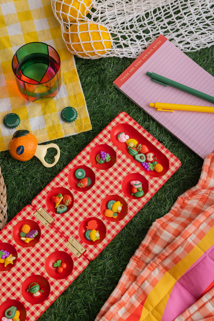 Red gingham mancala board with fruit shaped pieces.