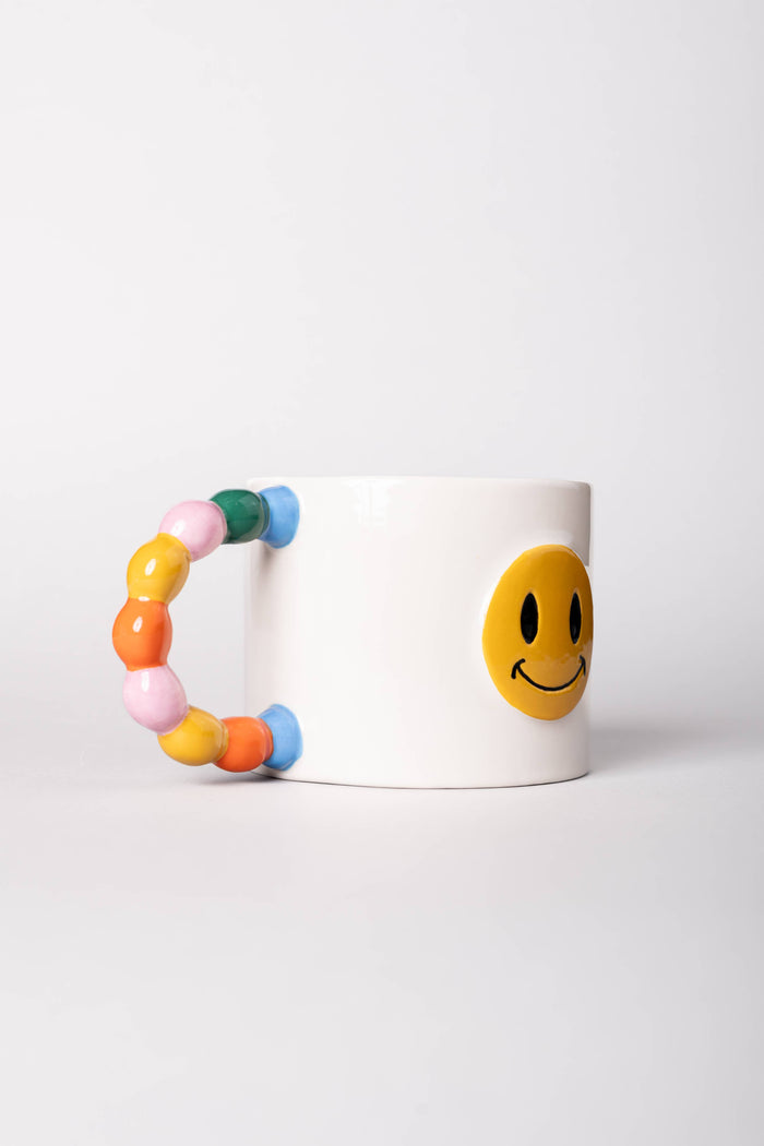 Colorful bead style handle on a mug with a smiley face design against a white background