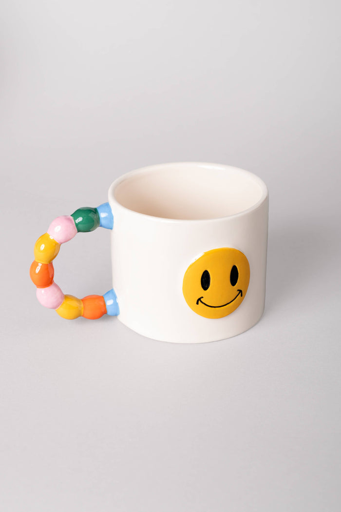 White mug with smiley face design and colorful handle on a light gray background