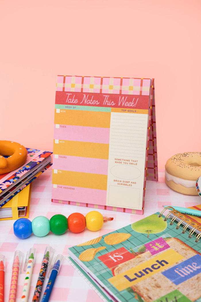 Colorful notepads and stationery items on a pink surface with donuts.