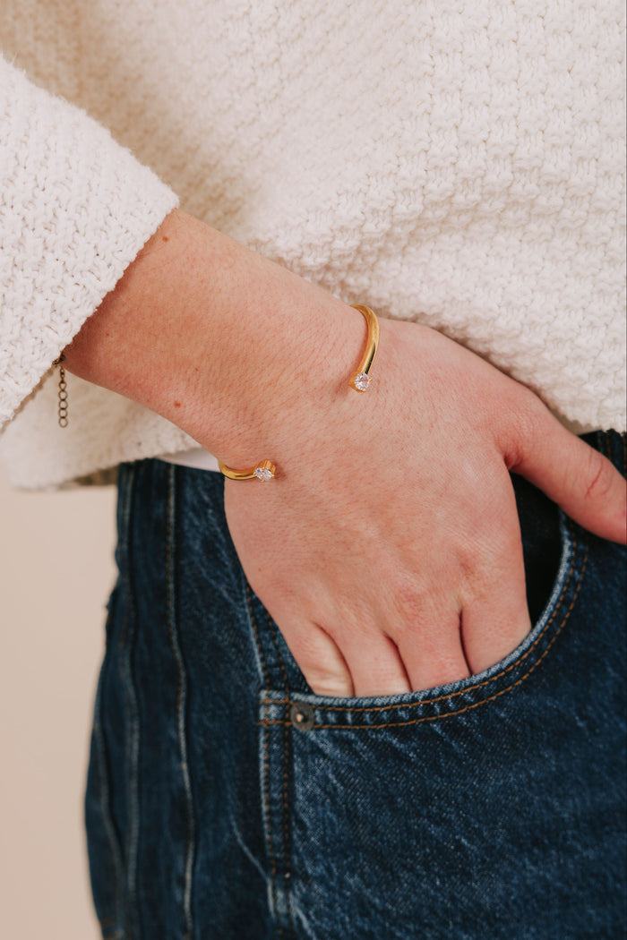 Hand with gold bracelet in a pocket, wearing a white coat