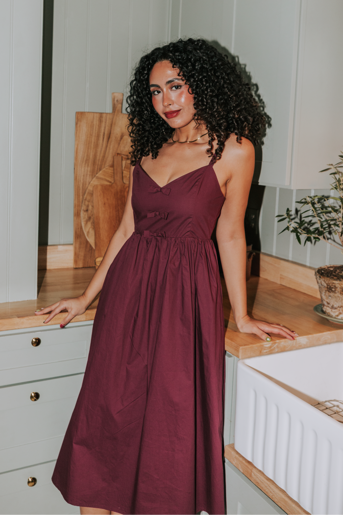 Woman in a burgundy dress standing in a kitchen.