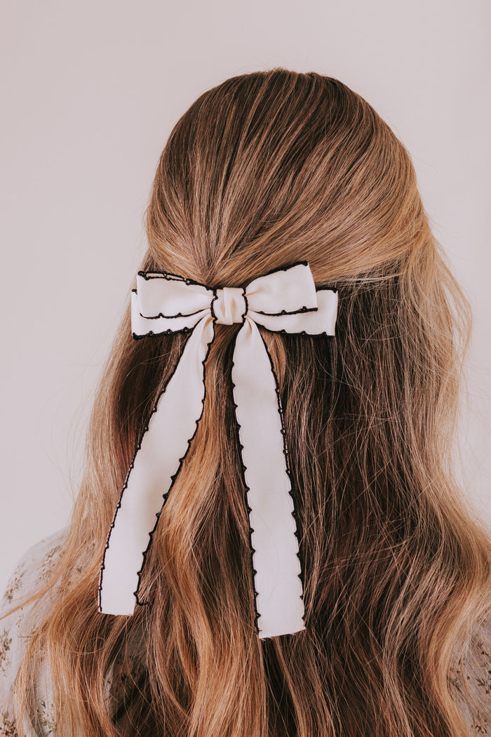 White hair bow in long, wavy brown hair against a neutral background