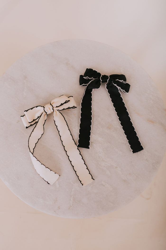 Two hair bows, one white and one black, on a marble surface.