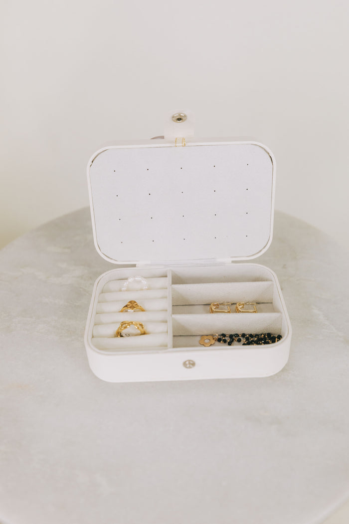 White jewelry box with gold rings and black beads on a white surface