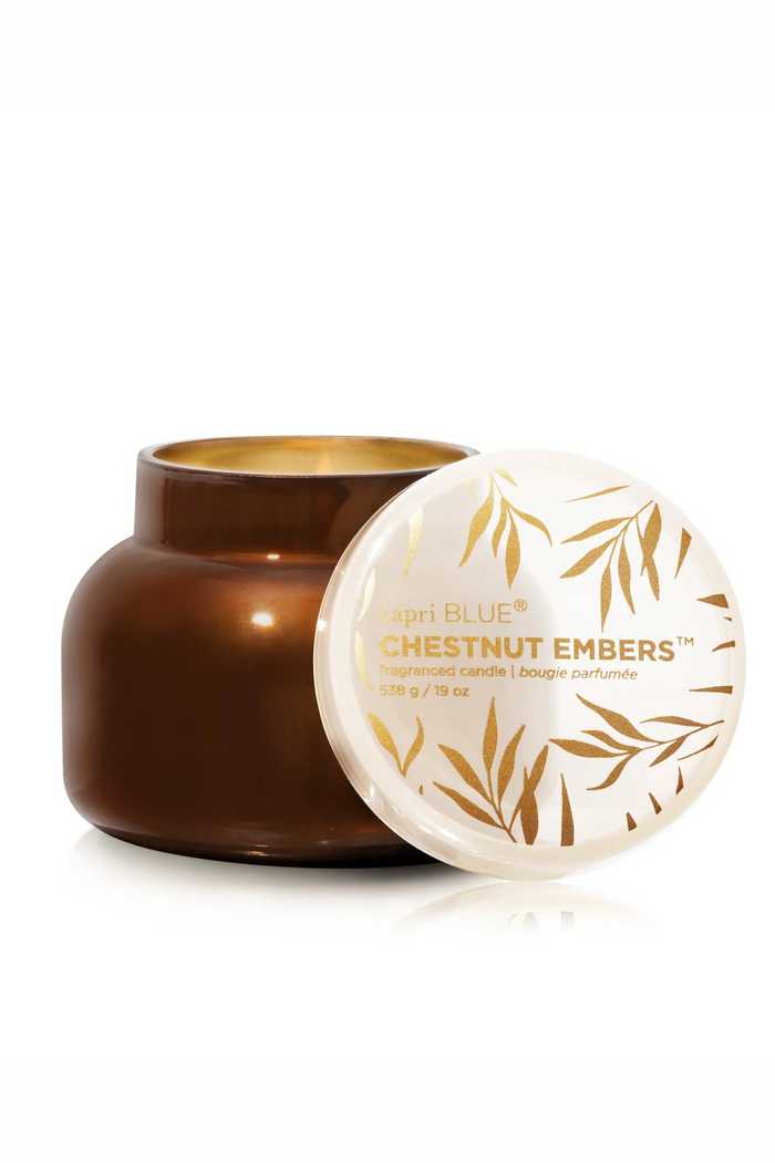Glass candle jar in coppery brown with a cream glass lid with gold accents in scent chestnut embers by capri blue.