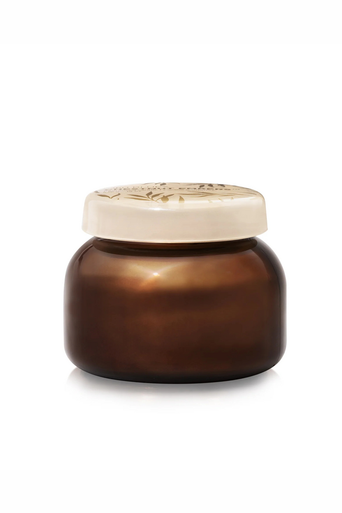 Glass candle jar in coppery brown with a cream glass lid with gold accents in scent chestnut embers by capri blue.