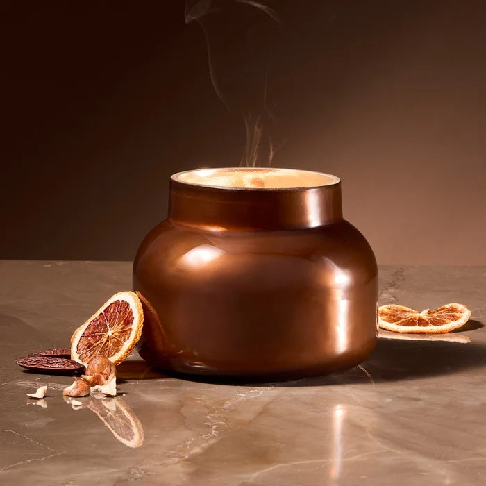 Bronze-colored glass candle jar with steam rising, surrounded by dried oranges.
