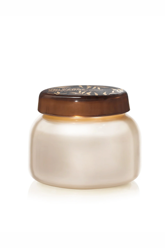 White pearlescent glass candle with brown glass lid with gold accents in volcano by capri blue.