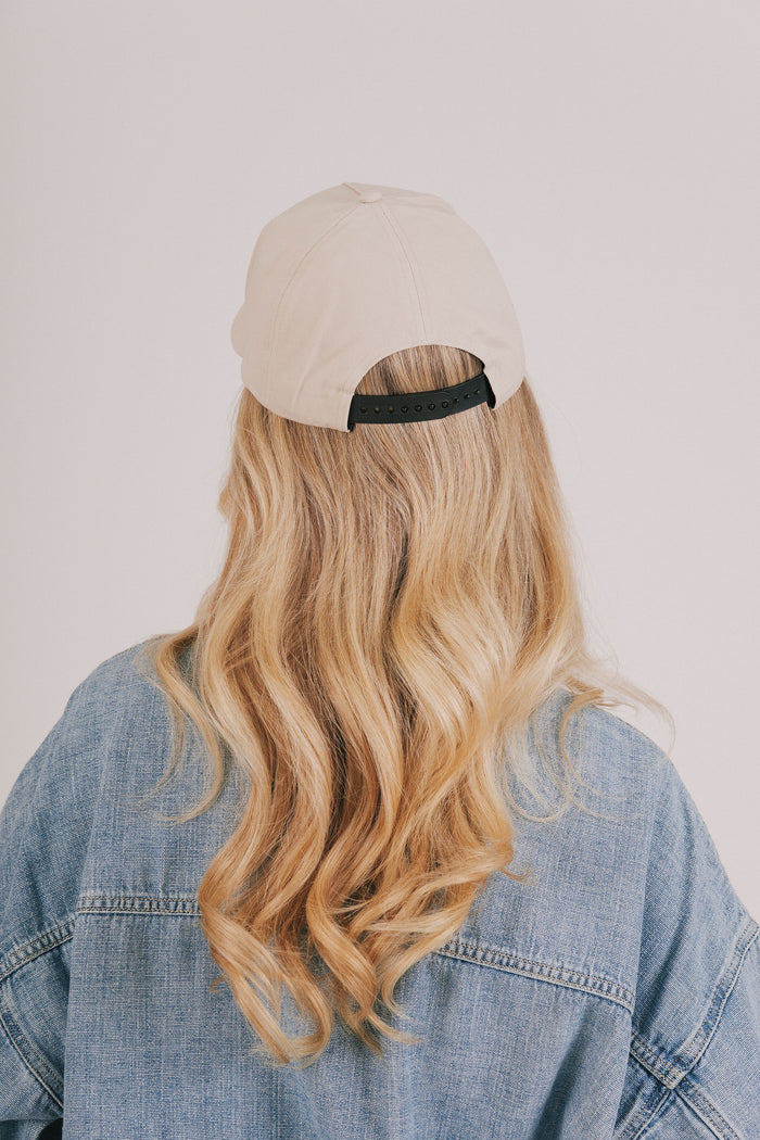 Person wearing a beige cap and denim jacket with long blonde hair on a plain background