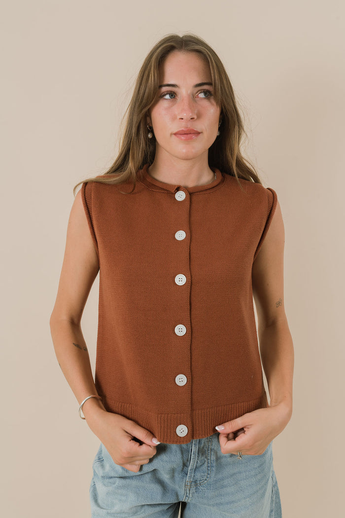 Woman wearing a brown sleeveless button-up top against a beige background