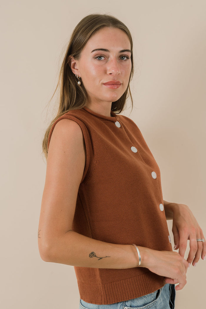 Woman wearing a brown sleeveless top with buttons against a beige background