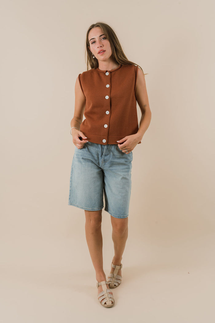 Woman wearing a brown sleeveless top with buttons and light blue shorts on a beige background