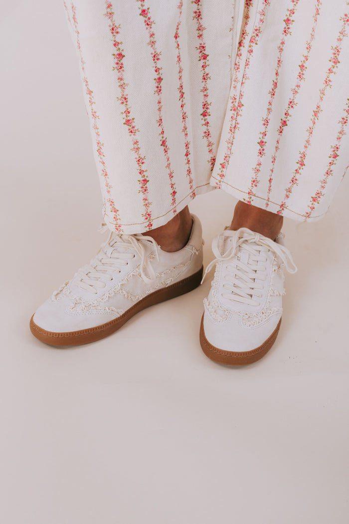 White sneakers with brown soles worn with white pants featuring red floral patterns on a light background