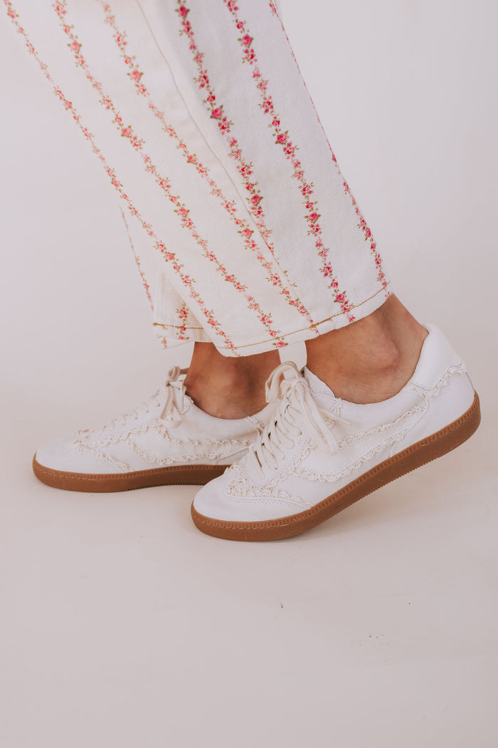 White sneakers with brown soles worn with white pants featuring red patterns on a light background