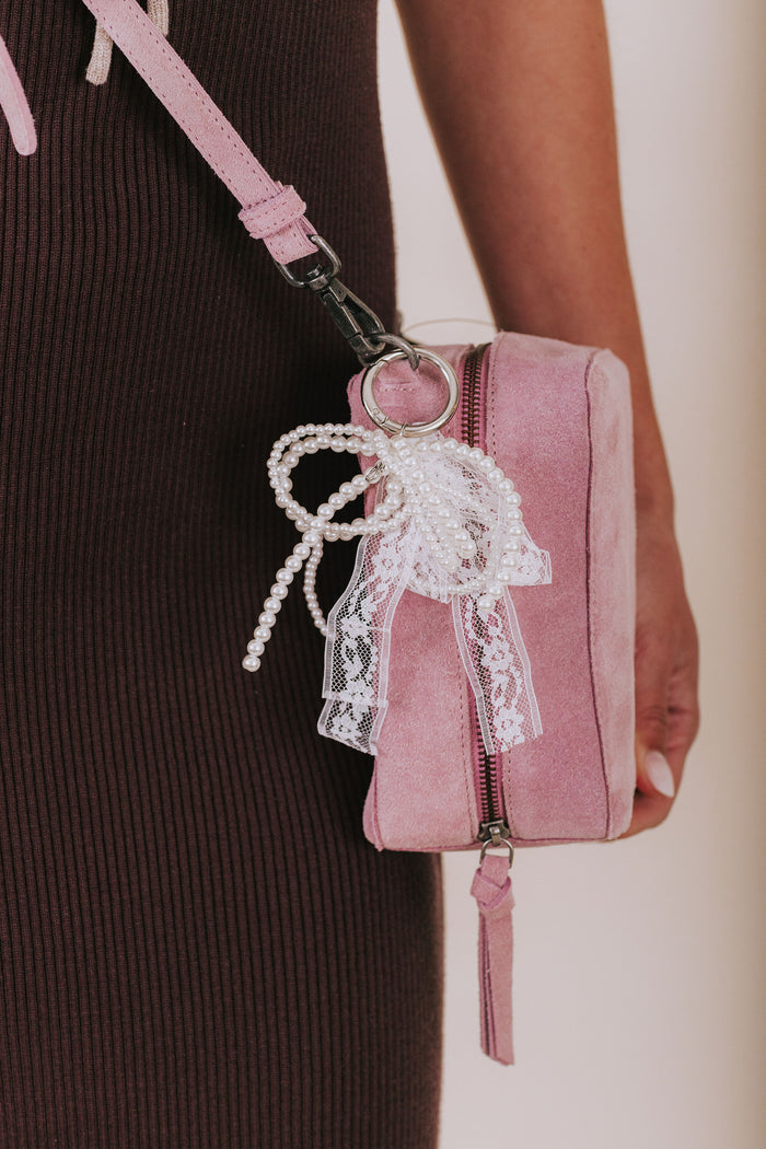 Pink handbag with lace detail held by a person wearing a dark ribbed sweater.