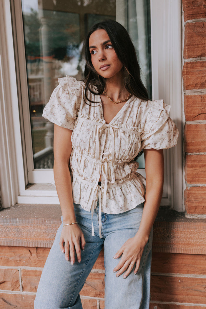 White blouse with floral pattern, ruching, tie front, and puff sleeves with a v neckline.