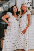 Two women in white polka dot dresses standing in a room with a fireplace.