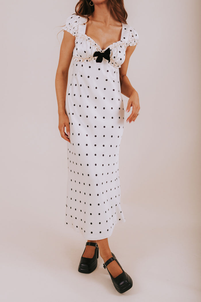 Woman wearing a white dress with black polka dots and a bow on a plain background