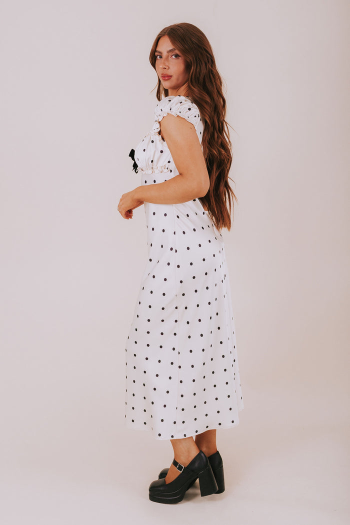 Woman wearing a white dress with black polka dots against a plain background