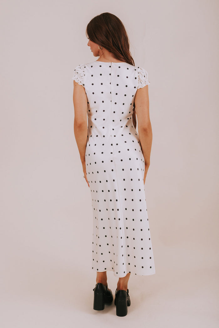 Woman wearing a white dress with black polka dots against a plain background