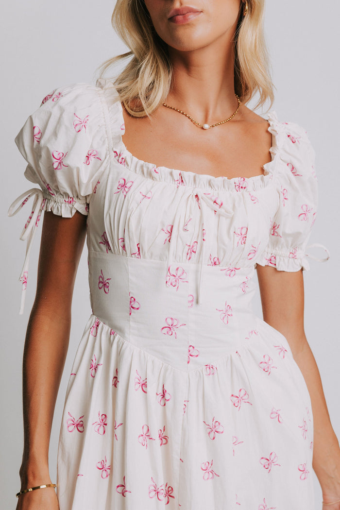 white midi dress with pink bow print and ruched bust and puff sleeves close