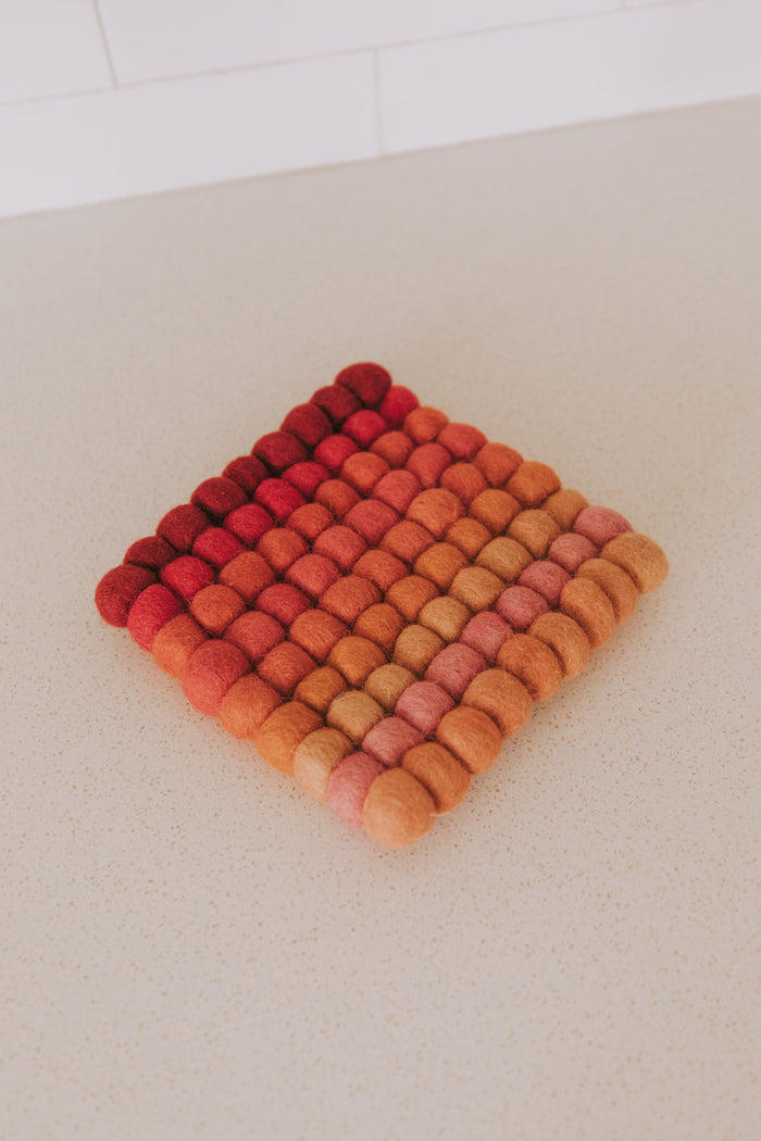 Wool felt ball trivet with a gradient of red, orange, and pink colors on a light background