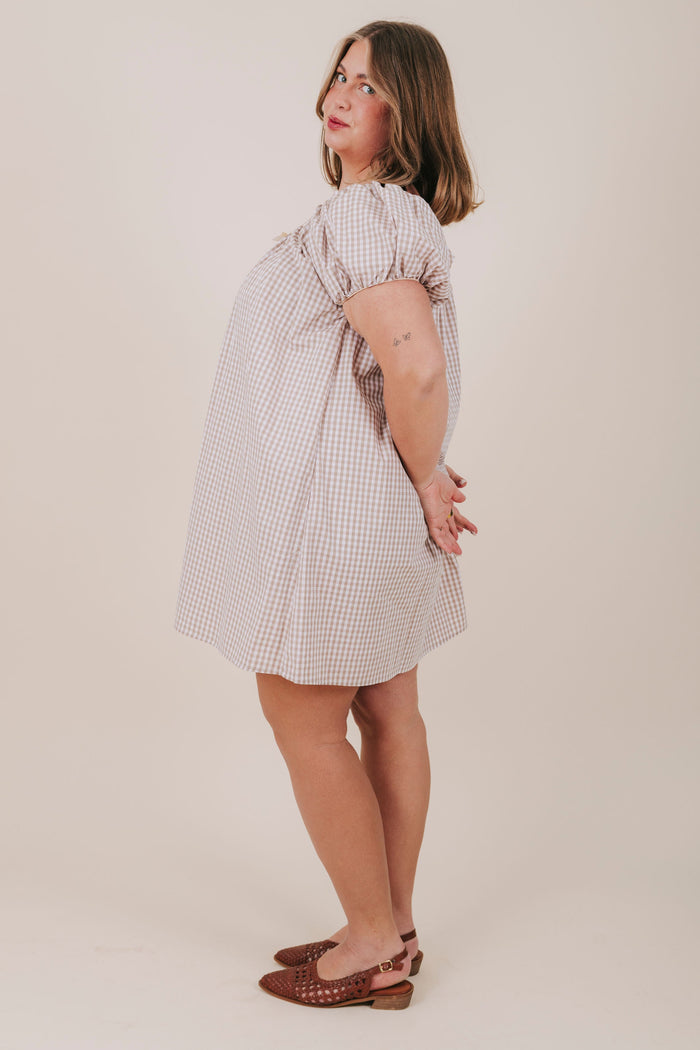 white and tan gingham dress with round neckline, bubble sleeves, and a bow detail. Mini-knee length