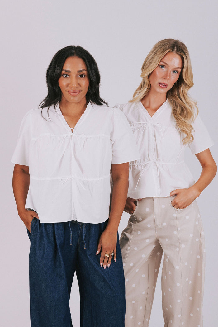 White plus size blouse with short sleeves and ruffled trim. Open front with drawstring tied bow closure