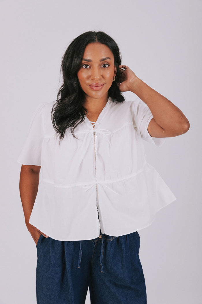 White plus size blouse with short sleeves and ruffled trim. Open front with drawstring tied bow closure