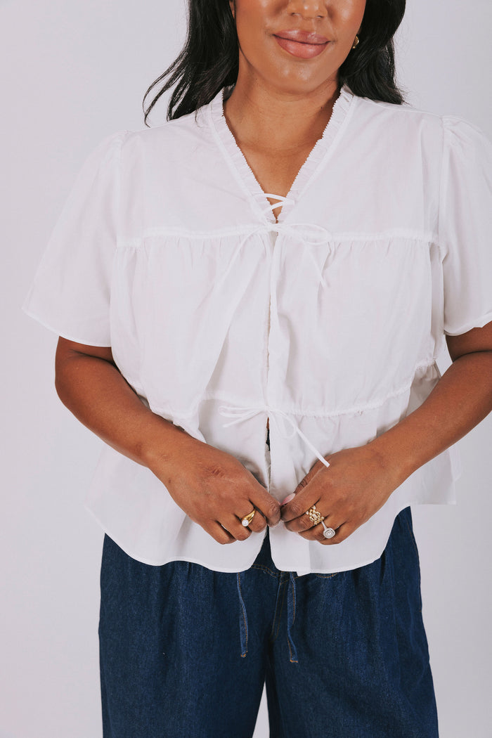 White plus size blouse with short sleeves and ruffled trim. Open front with drawstring tied bow closure