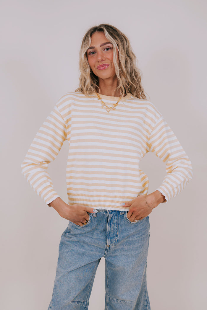 Woman wearing a yellow and white striped sweater and jeans against a plain background