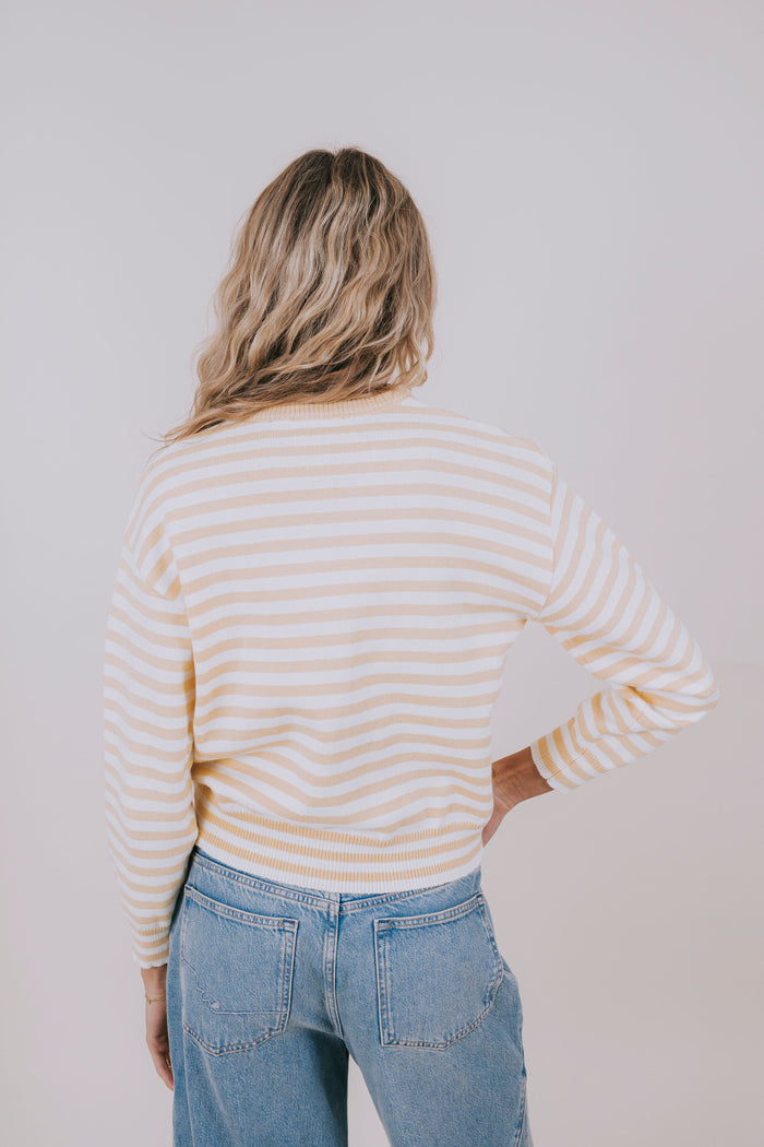 Person wearing a striped sweater and jeans against a plain background