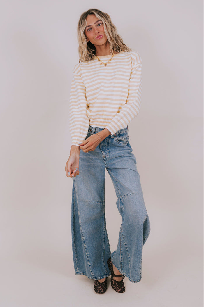 Woman wearing a striped sweater and blue jeans against a plain background