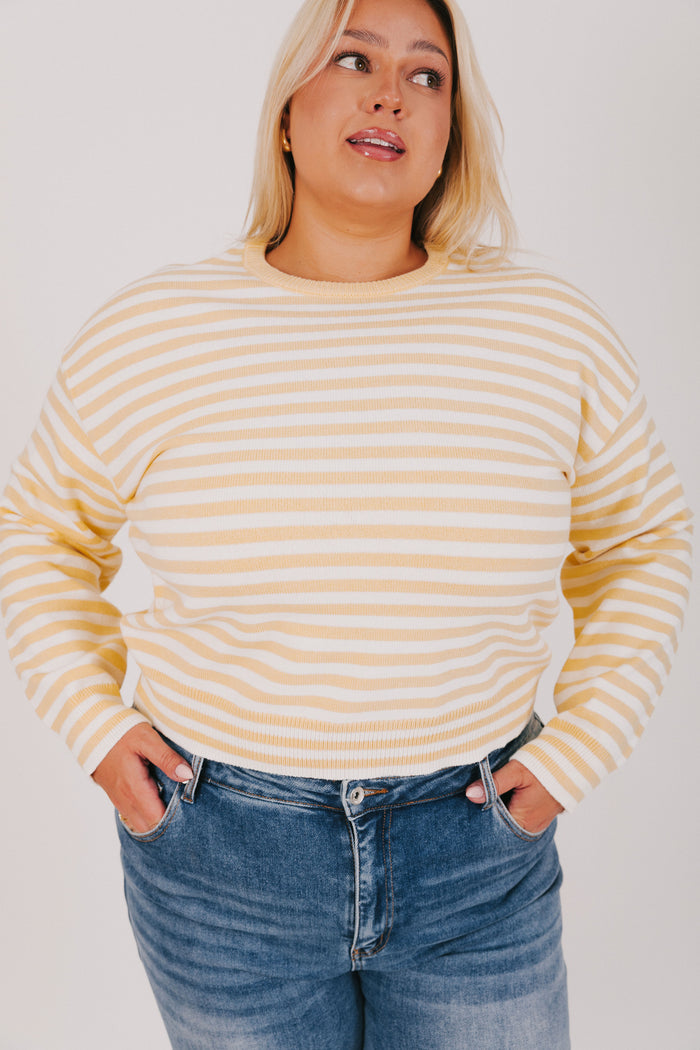 Woman wearing a striped sweater and blue jeans against a plain background