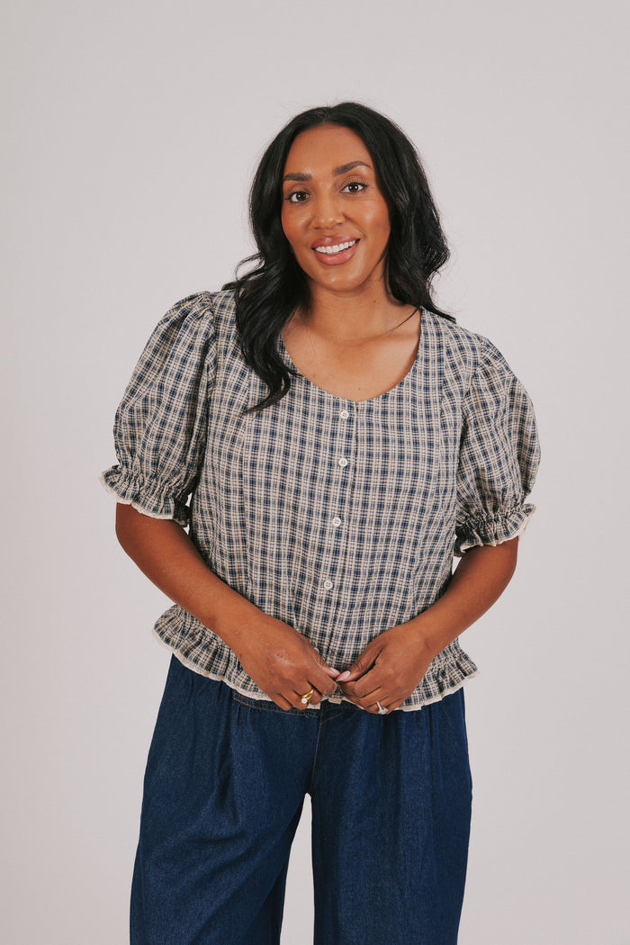 Plus size plaid navy blouse with button up front and short puff sleeves. Round neckline and ruffle hem.