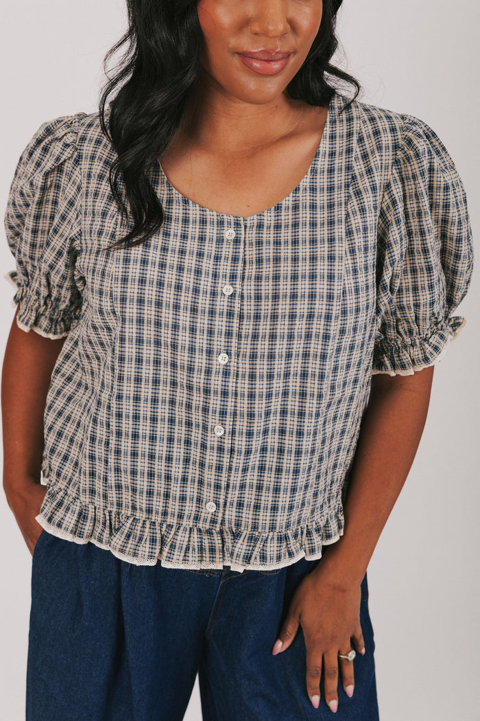 Plus size plaid navy blouse with button up front and short puff sleeves. Round neckline and ruffle hem.
