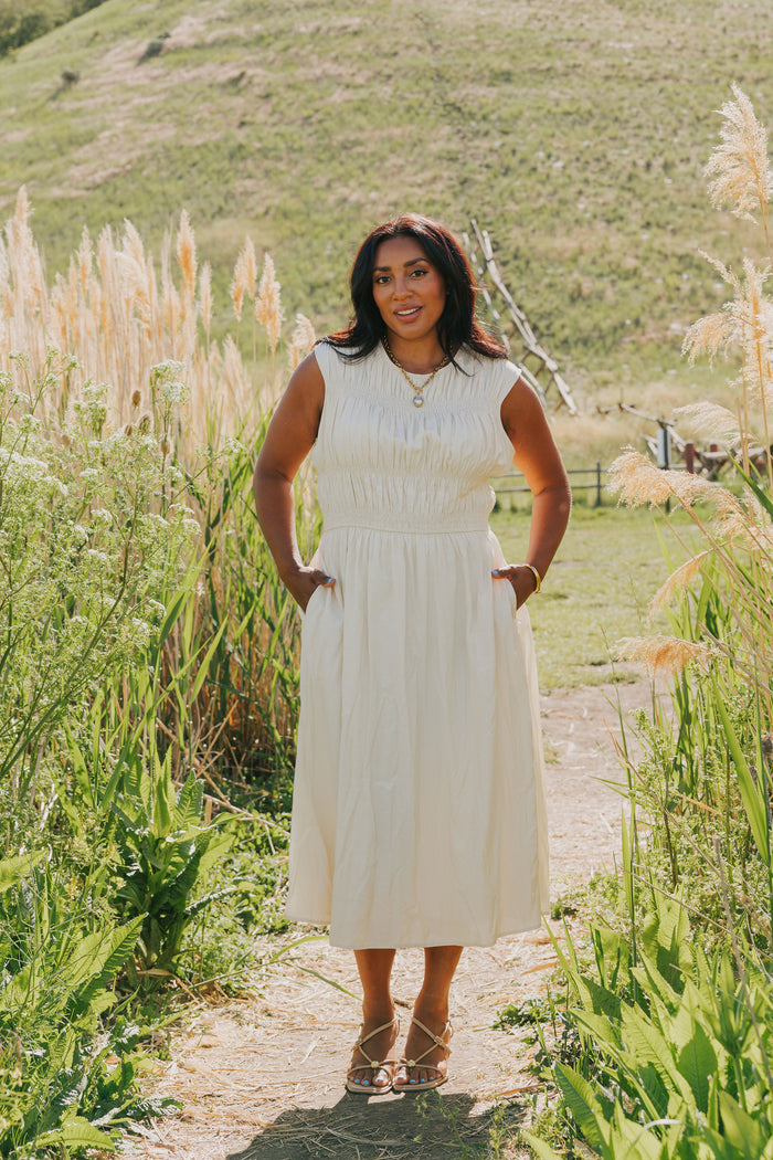 Woman in a white dress standing in a natural setting with tall grass and a hill in the background