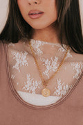 Close-up of a person wearing a gold necklace with a pendant on a sheer lace garment.