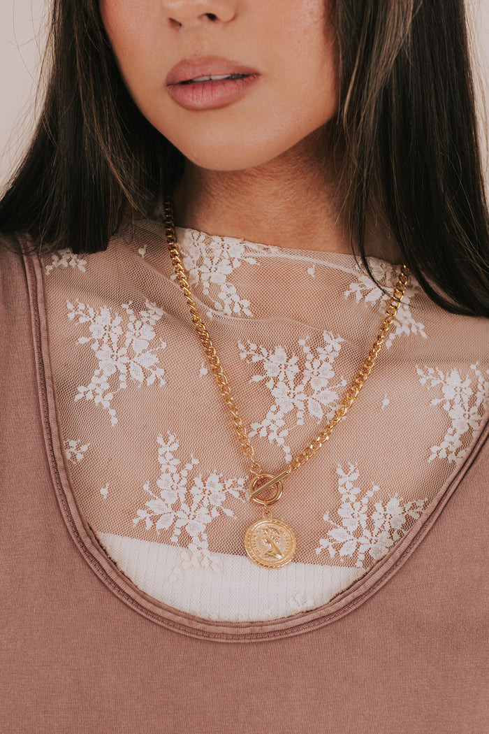 Close-up of a person wearing a gold necklace with a pendant on a sheer lace garment.