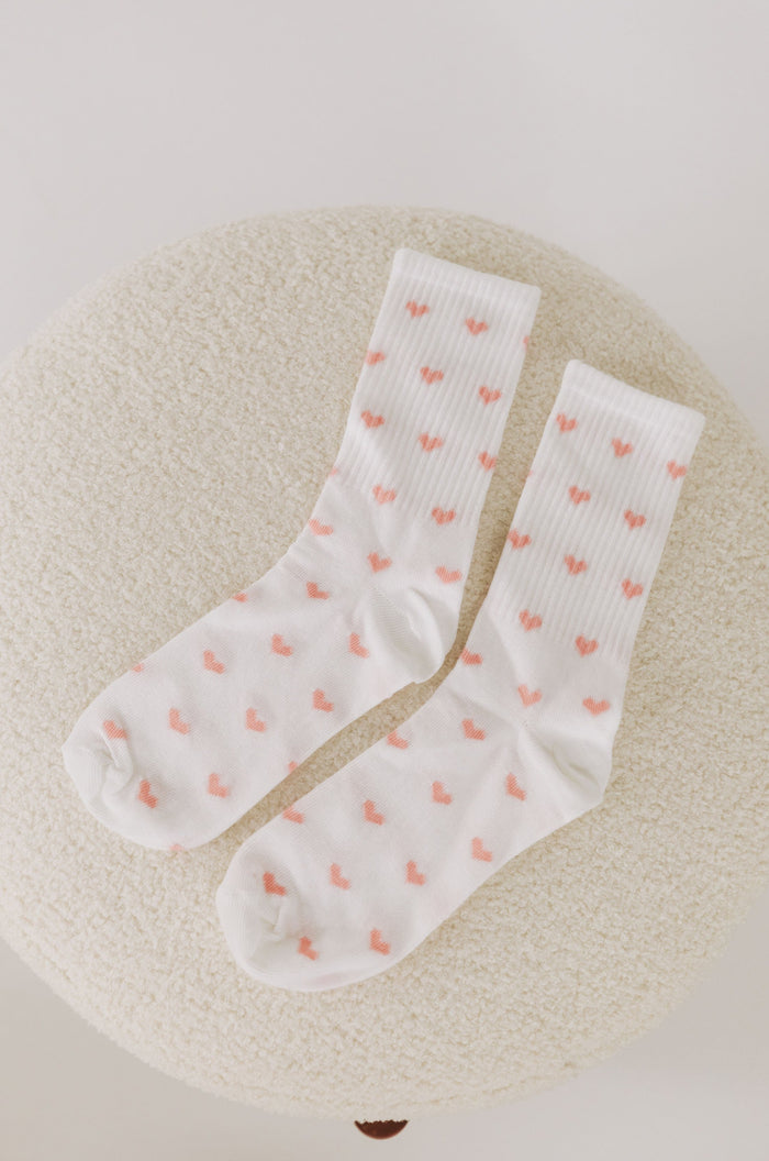 White socks with pink heart patterns on a textured beige surface