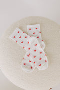 A pair of white crew socks with a small red heart pattern displayed on a neutral surface.