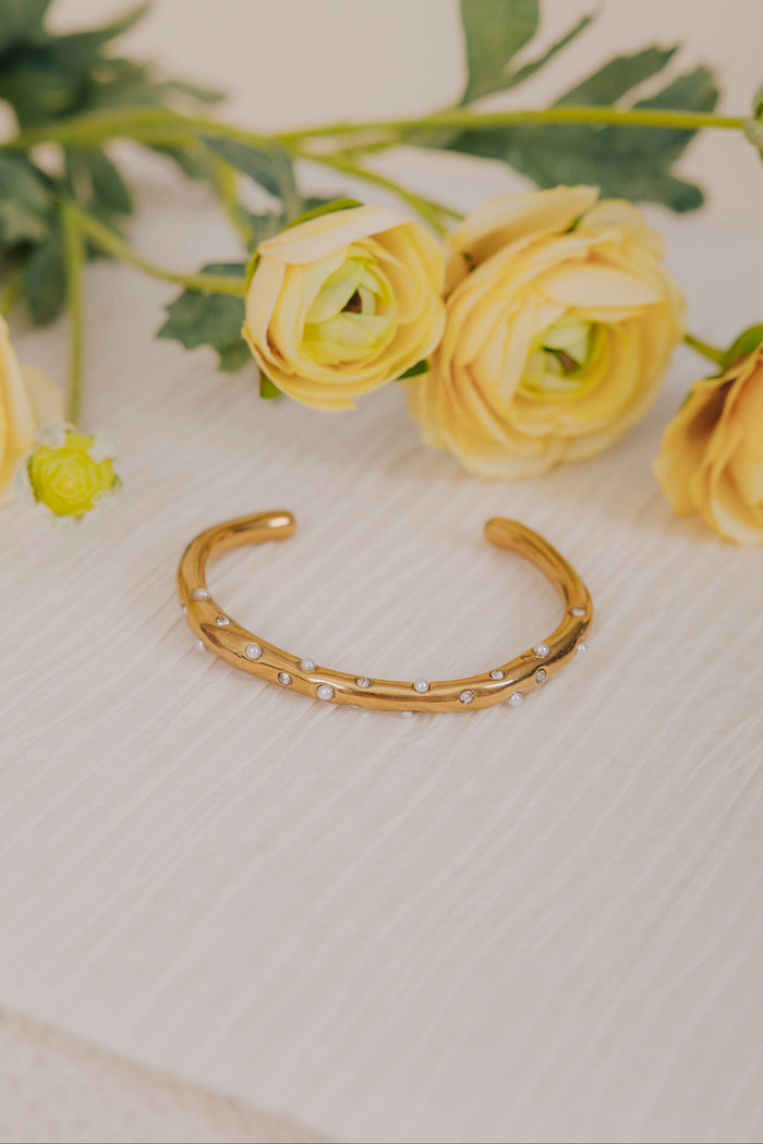 Gold bracelet on a textured surface with yellow flowers in the background
