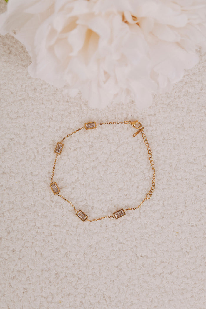 Gold bracelet with square charms on a textured beige surface