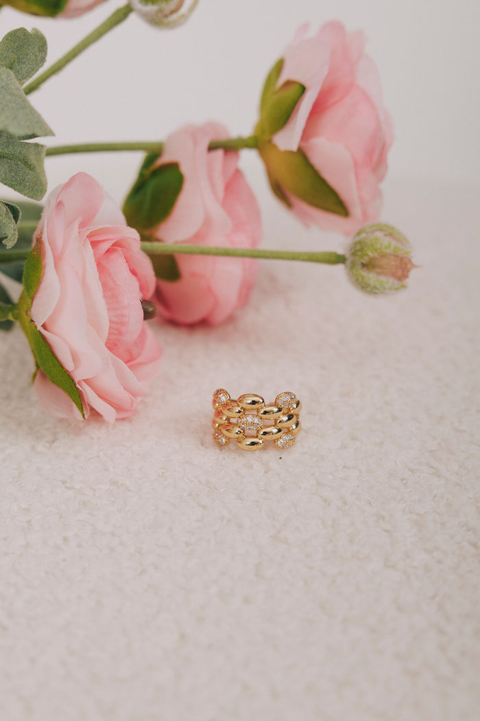 Gold ring on a textured surface with pink flowers in the background